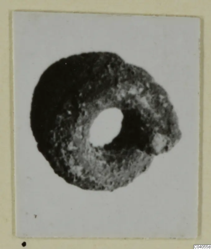 Ring-shaped bronze personal adornment with a large central hole, photographed on a mounted card