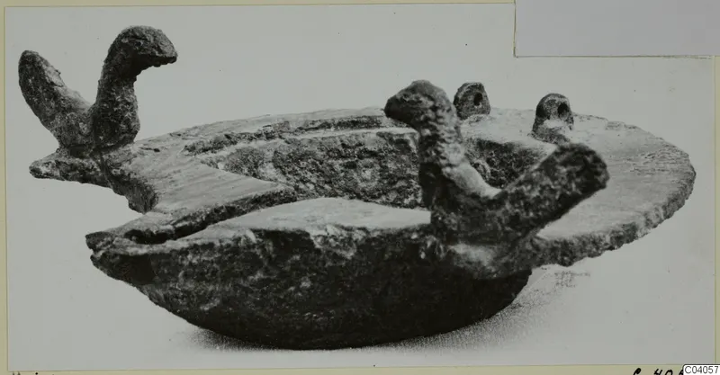 Corroded metal lamp with a shallow body and two bird-head shaped projections on its rim