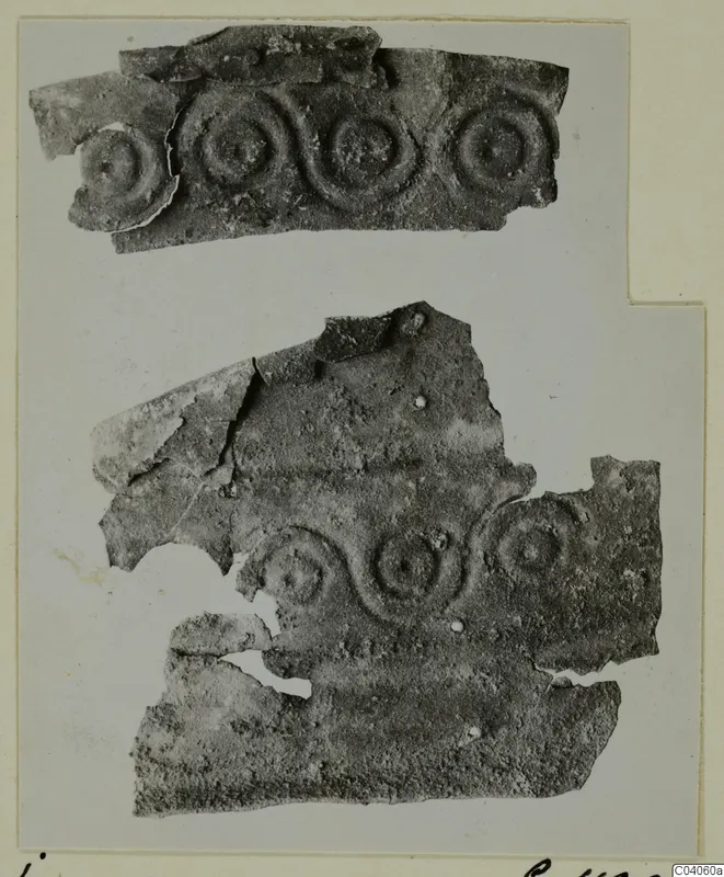 Two fragments of thin corroded metal sheet decorated with rows of raised concentric circles, mounted on a card.