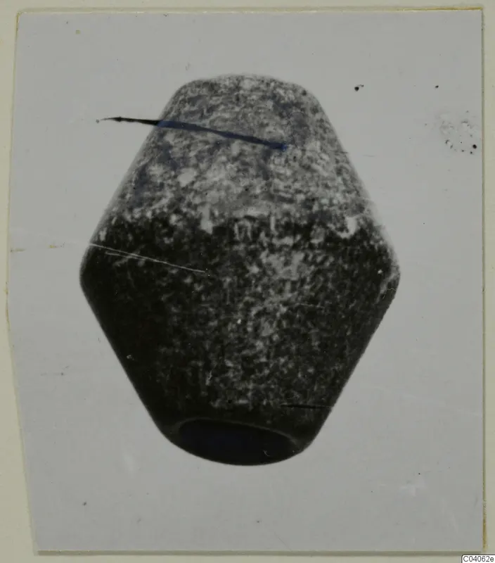 Faceted stone object with a hole in its base, photographed against a pale card background