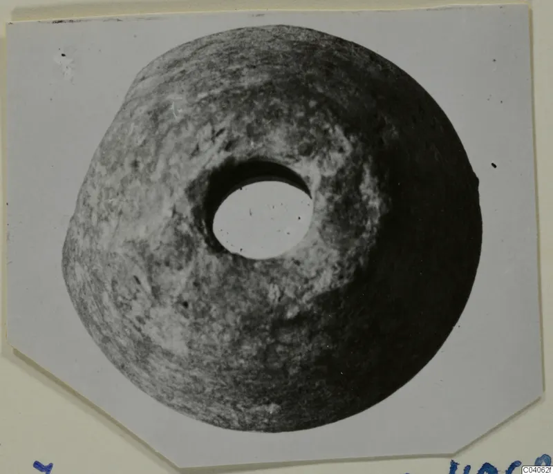Disc-shaped stone object with a large central hole, shown in a photograph mounted on a card