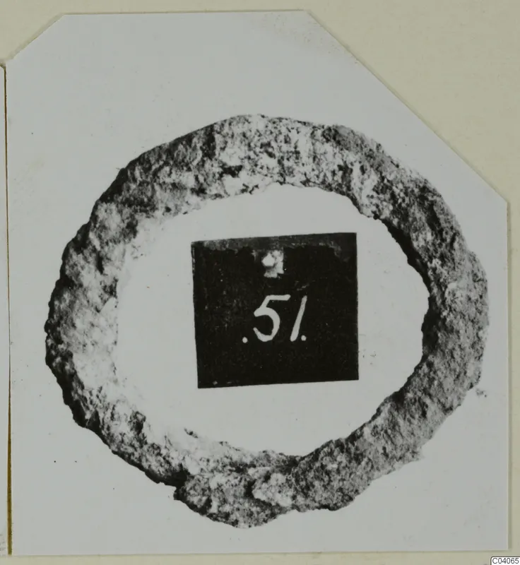 Corroded ring-shaped metal object on a white card, with a black number label placed in its centre