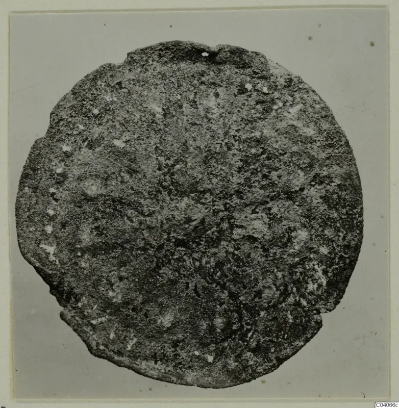 Corroded round metal disc with a small hole at its upper edge, photographed face-on on a grey background.