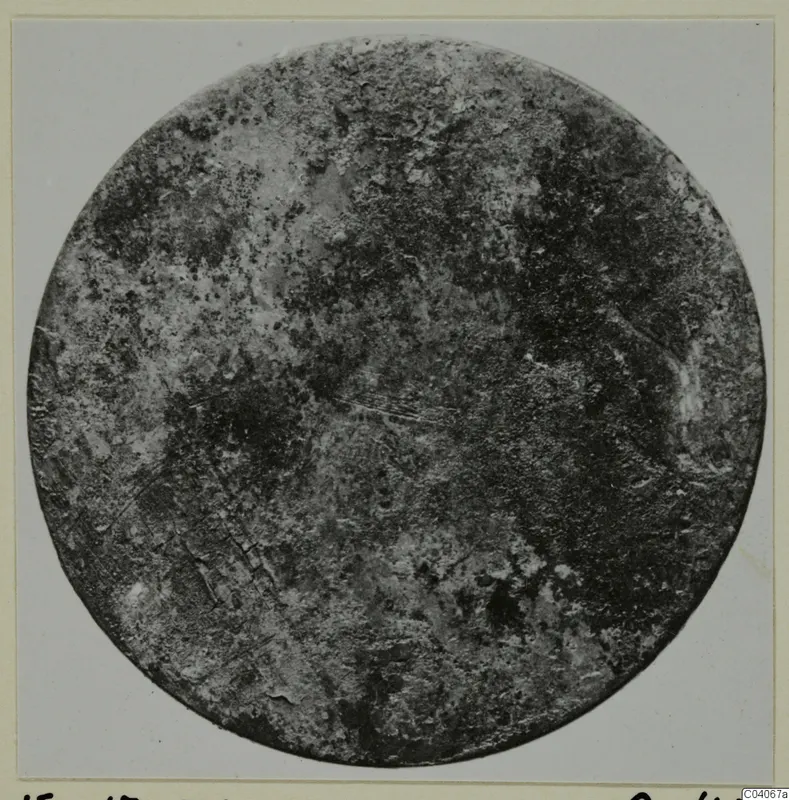 Corroded round disc photographed face-on, a find from Enkomi Tomb 17