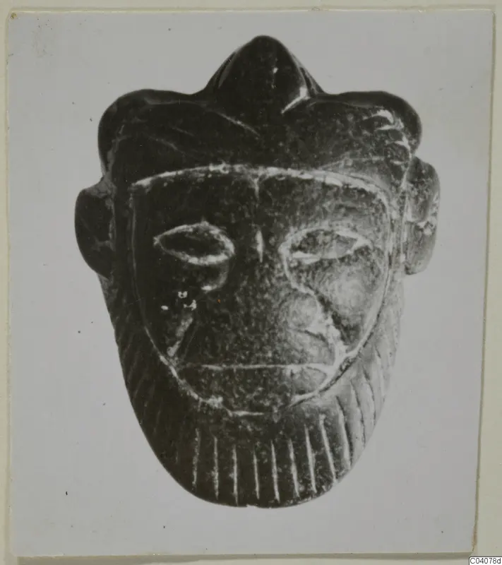 Dark stone face-shaped object with a pointed crest, projecting ears and almond-shaped eyes.