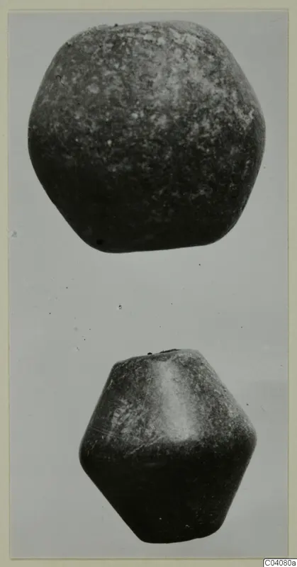 Two dark stone objects, one rounded and one faceted, photographed one above the other against a grey background.