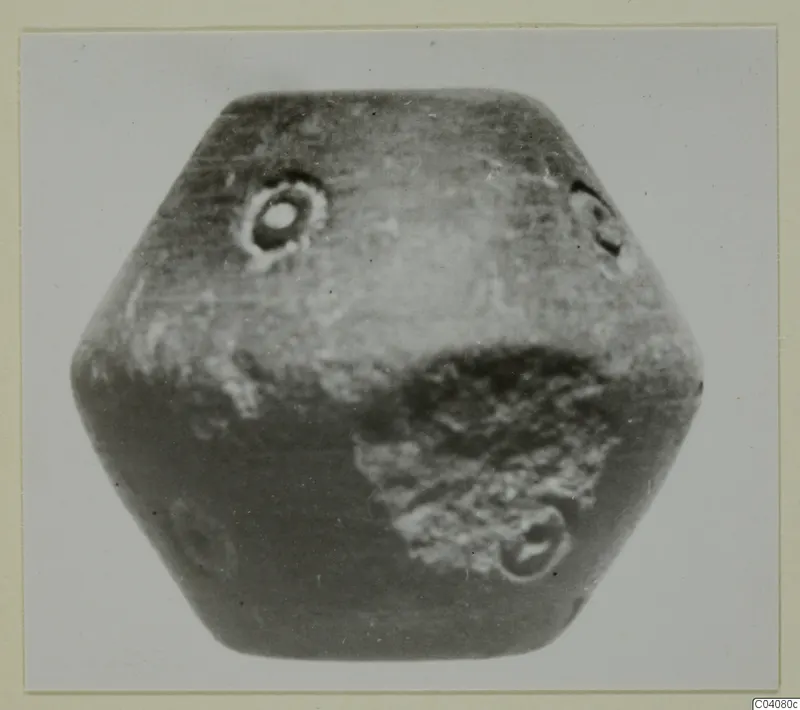 Hexagonal stone object with small circular perforations, photographed against a pale background.