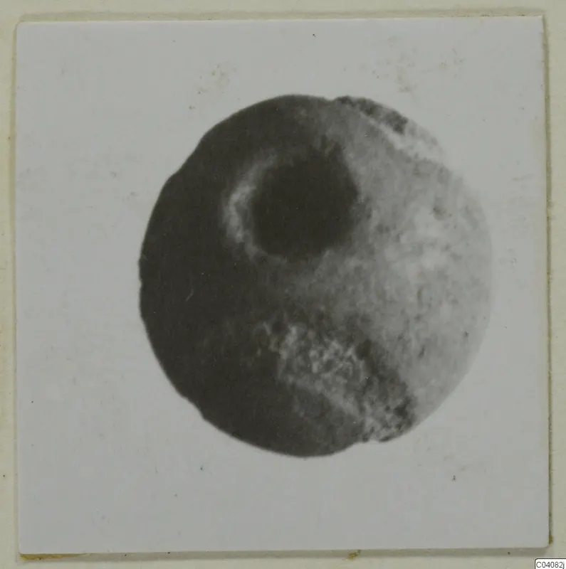 Round stone object with a large central hole, shown face-on in a photograph mounted on card