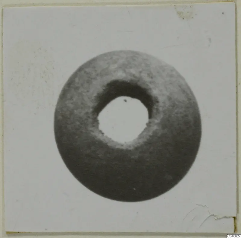 Round stone object with a large central hole, seen face-on against a pale background.