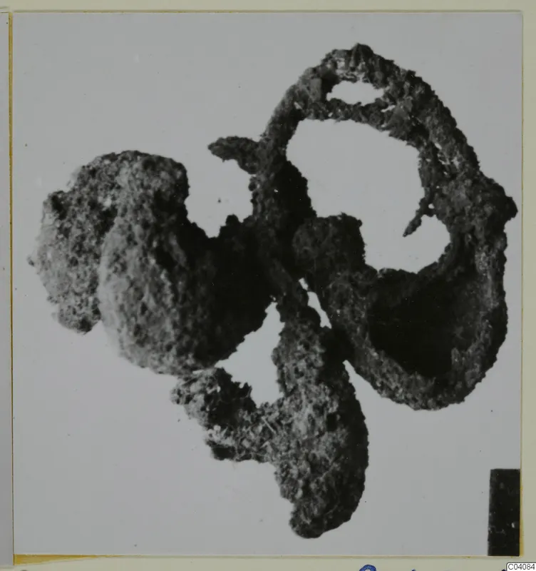 Corroded silver find: a lumpy, encrusted mass of metal with loops and open gaps, photographed on a pale background.