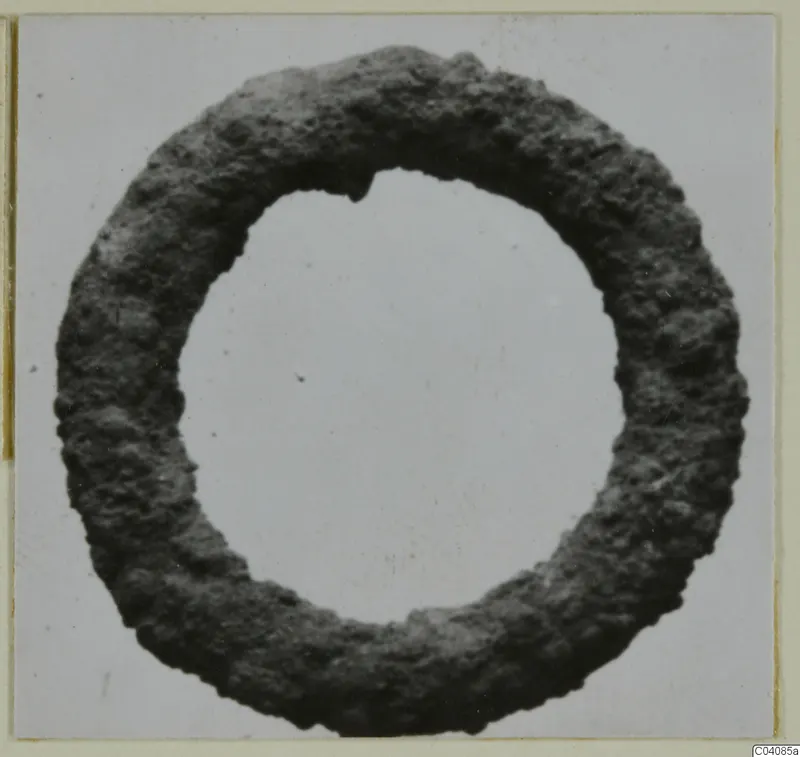 Corroded metal ring with a pitted, dark surface, photographed face-on against a pale background.