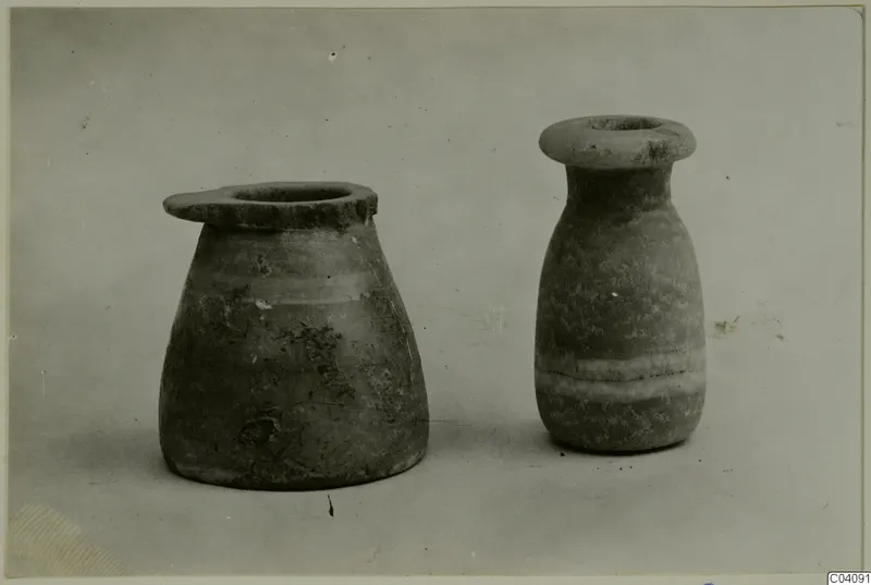Two stone vases with flared rims, one squat and one tall, photographed side by side on a plain grey backdrop.