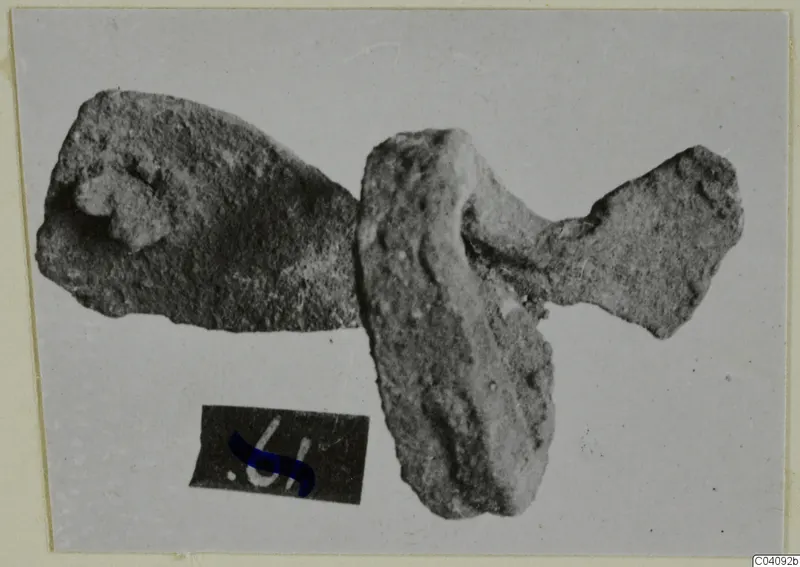 Two corroded bronze mounting fragments on a plain grey background, with a small number label below