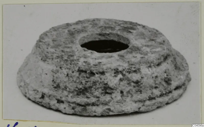 Squat grey object with a large round central hole and a ridged, stepped edge, photographed on a pale background