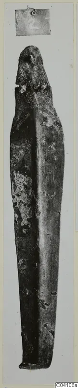 Bronze tool from Ayios Iakovos, long and narrow, photographed upright with a corroded green-brown surface