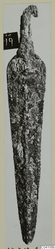 Corroded metal blade with a tapering point and a hooked projection at the top, photographed upright.