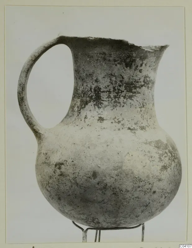 Pottery jug with a single loop handle and a broken rim, standing on a wire stand