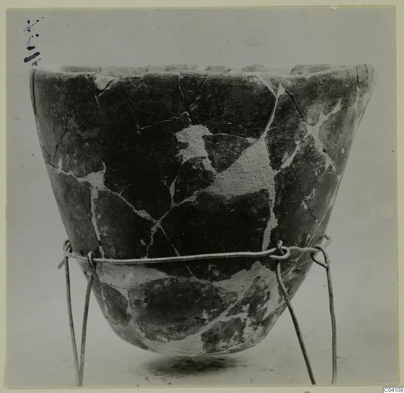 Pieced-together pottery vessel with a wide mouth, shown on a wire stand.
