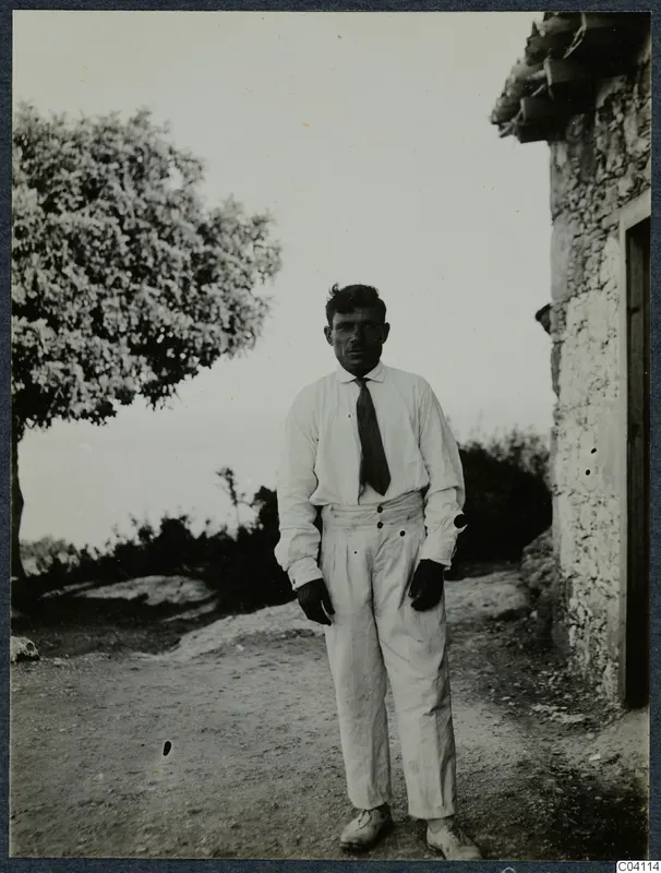 Sofoklis, known as Mavrokeratas, digger at Vouni Palace, standing beside a stone building on a dirt track