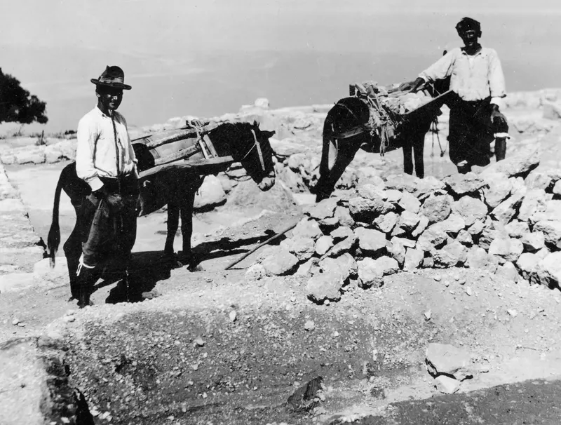 Two men with laden donkeys beside a heap of rubble at the palace at Vouni