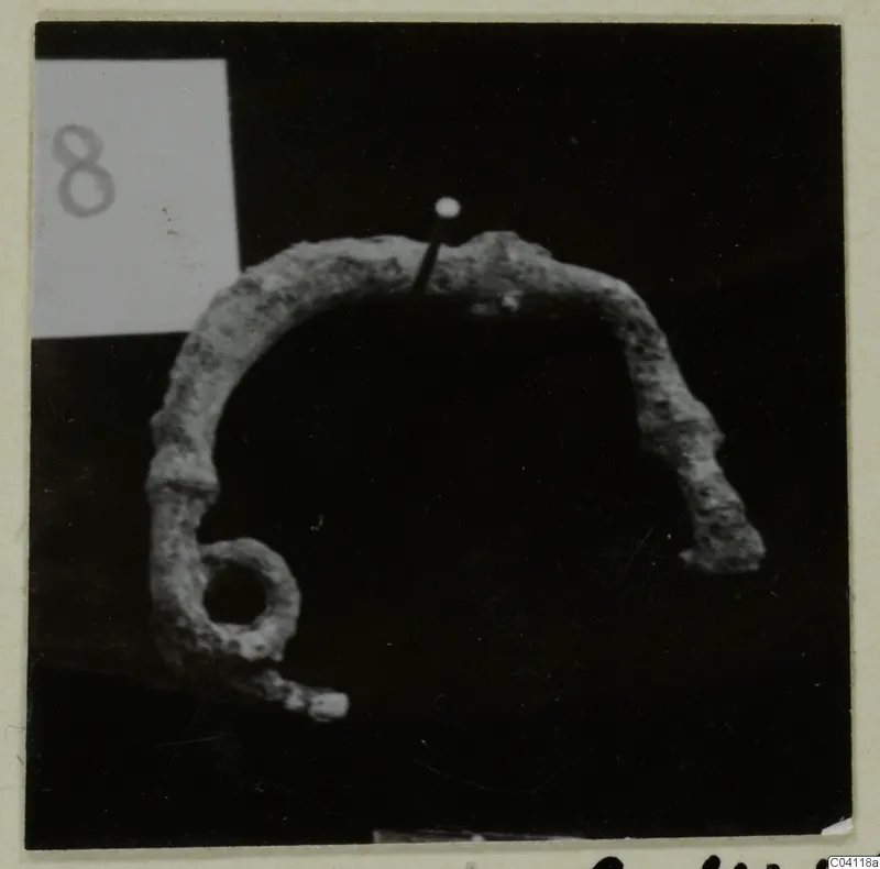Corroded bronze arched object with a round loop at one end, from Amathus tombs, shown against a black background