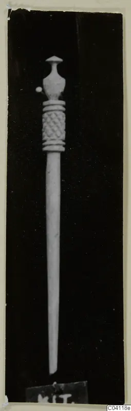 Bone pin with a carved lattice band below an ornate head, shown against a dark background