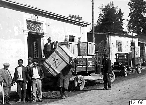 Crates of finds being loaded onto lorries in a Nicosia street, with several men standing by and one carrying a crate on his shoulder.