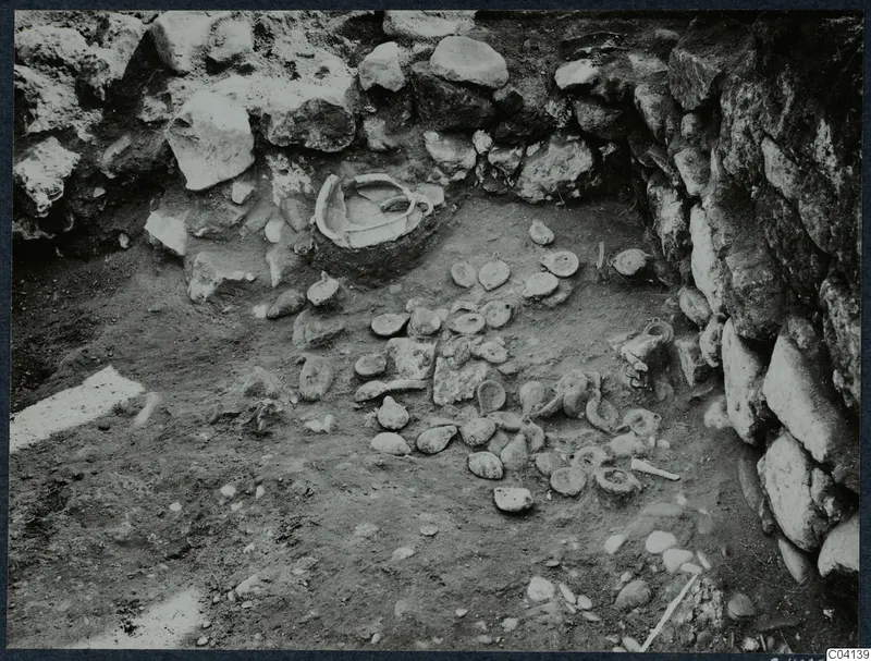 Finds in situ on the floor of an excavated area at Cholades, Soli, with a stone wall behind them.