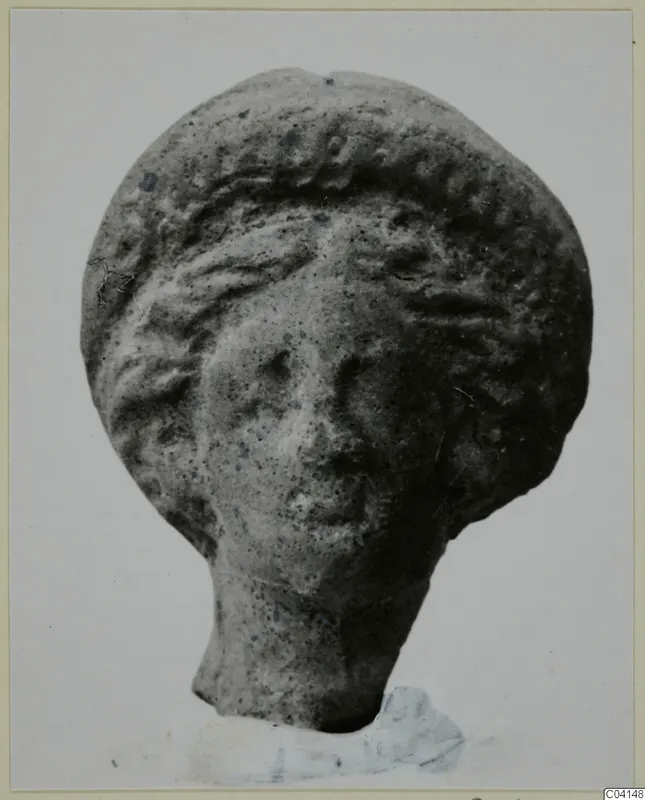 Terracotta figurine head with a wavy headdress and a short neck stub, photographed against a plain light background