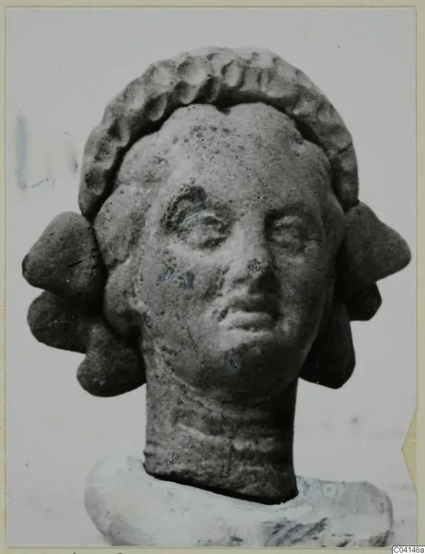 Terracotta female head with a curled hair band and side locks, shown against a plain background, from Soli.