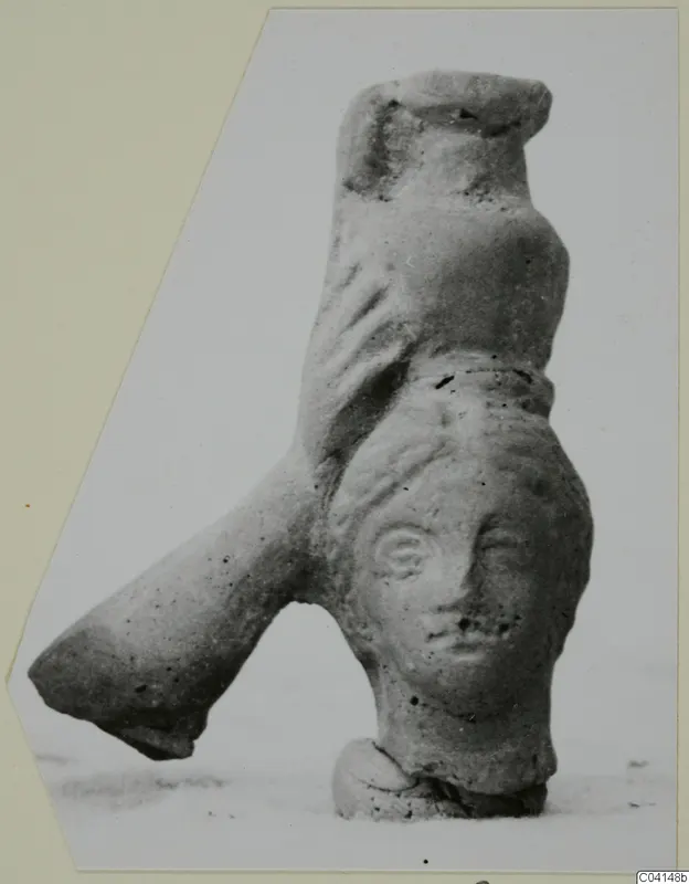 Terracotta figurine with a modelled human face, a tubular projection on the left and a small base