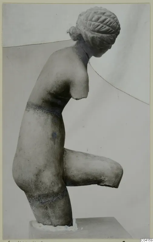 Marble sculpture of a female figure with hair in a bun, arms broken off, one leg bent up, on a block base