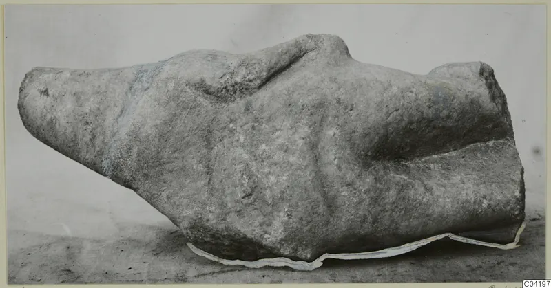 Marble sculpture fragment, a weathered pale stone piece lying on its side on a grey surface