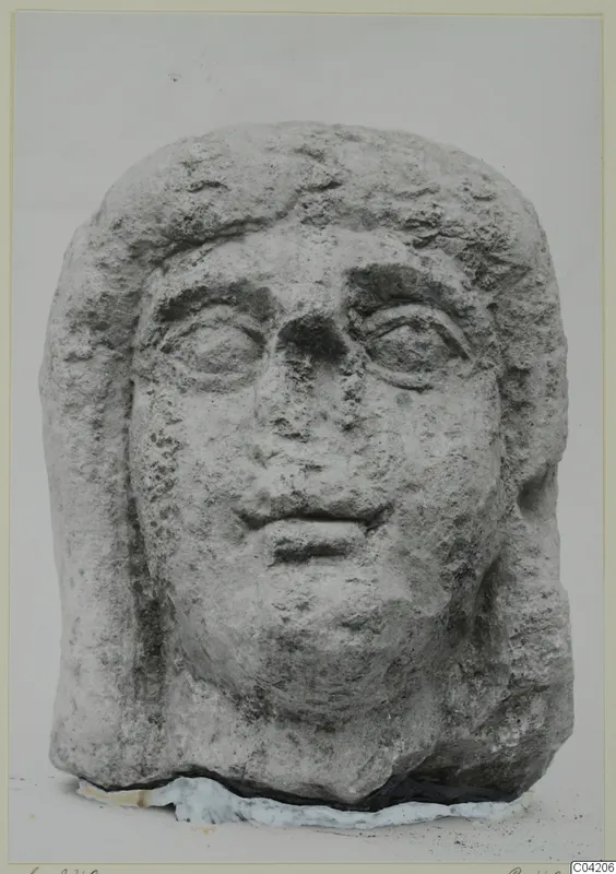 Carved stone head from Soli, frontal view, with hair framing the face and a rough, weathered surface.