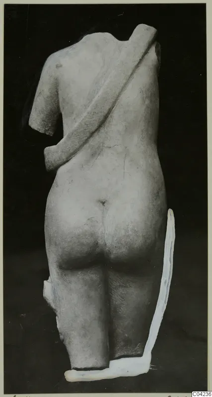 Back view of a headless marble statue with a broad diagonal band across the back, against a dark background