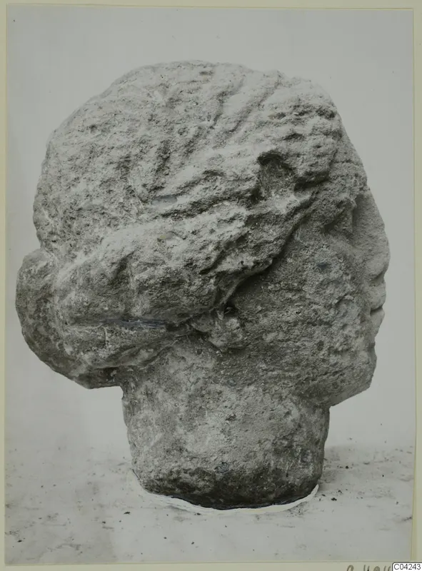 Stone head from Soli shown in right profile, with wavy hair swept back and a weathered, pitted surface.