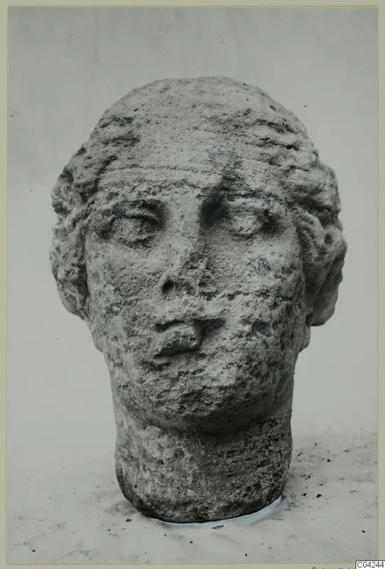 Stone female head with a broad face and hair framing it, photographed against a plain background