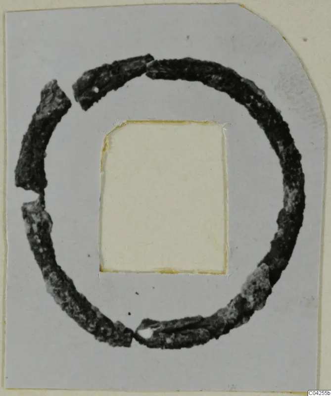 Corroded bronze ring made of several broken pieces, mounted on a grey card with a cut-out window, Milia