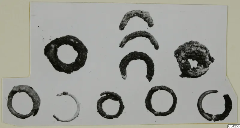 Bronze personal adornments from Milia: ten corroded metal rings and curved fragments laid out on a white card