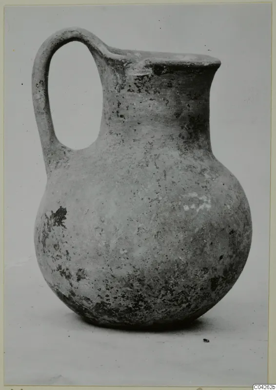 Round-bodied jug with a strap handle and flared rim, photographed against a plain background, from Milia.