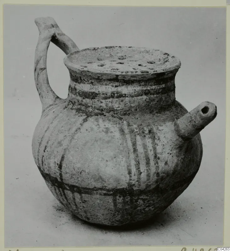 Pottery vessel from Milia with a strap handle, a short side spout and a perforated rim, decorated with dark painted bands