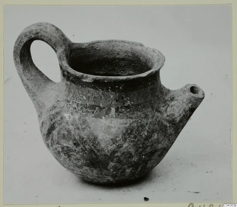 Pottery jug with a looped handle, a spout and painted bands, photographed on a plain surface.
