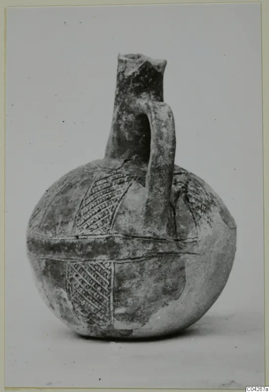 Round jug with a tall neck, strap handle and incised hatched bands on the body, Black Slip Ware, from Milia.