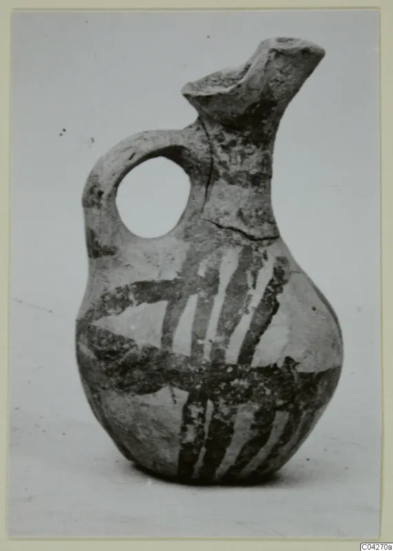 Pottery juglet from Milia with a beaked spout, loop handle and dark painted bands on a pale surface