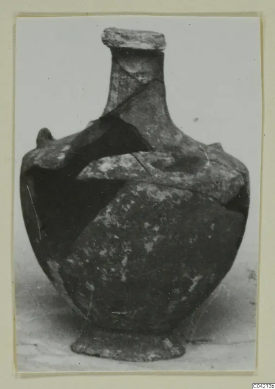 Pottery jar with a narrow neck, rounded body and low foot, pieced together from fragments, shown against a pale background.