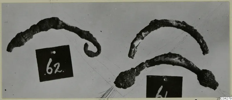 Three corroded bronze loops or bands photographed on a plain background, with two number labels beside them.