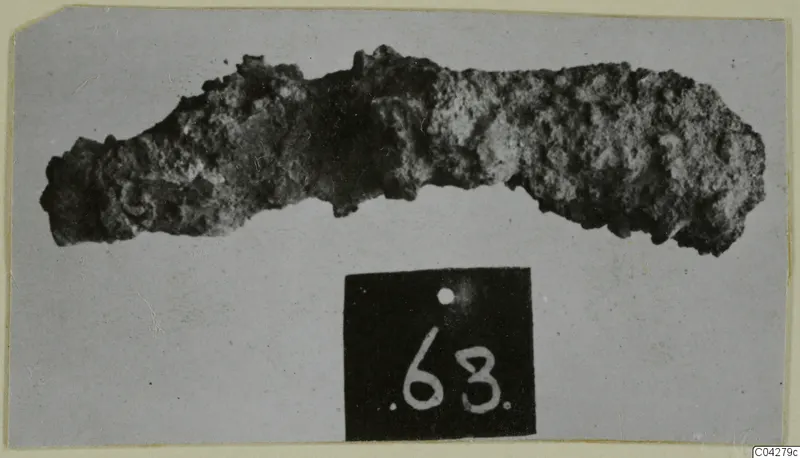 Heavily corroded iron object, elongated, photographed on grey card, from Amathus tombs