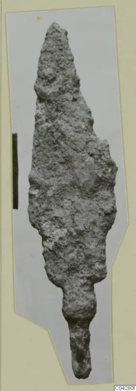 Corroded iron weapon blade from Amathus, leaf-shaped with a tapering tang, shown on a grey card mount.