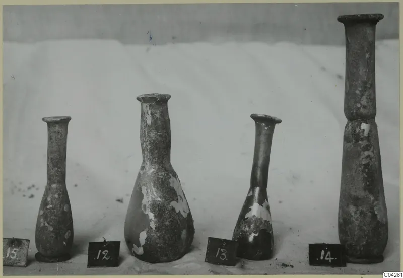 Four blown glass bottles of varying height, numbered 12 to 15, standing in a row on a pale cloth.