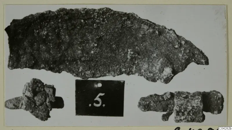 Three corroded metal objects from Amathus, tombs 2–26, photographed beside a dark number label